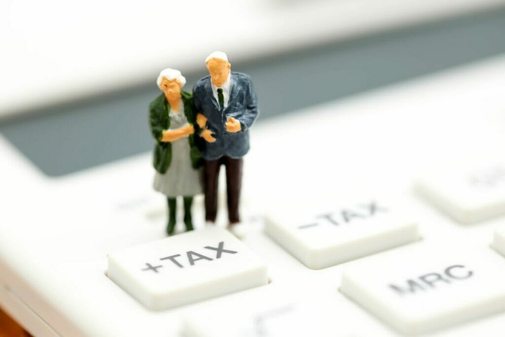 model of old couple standing on a calculator with tax button