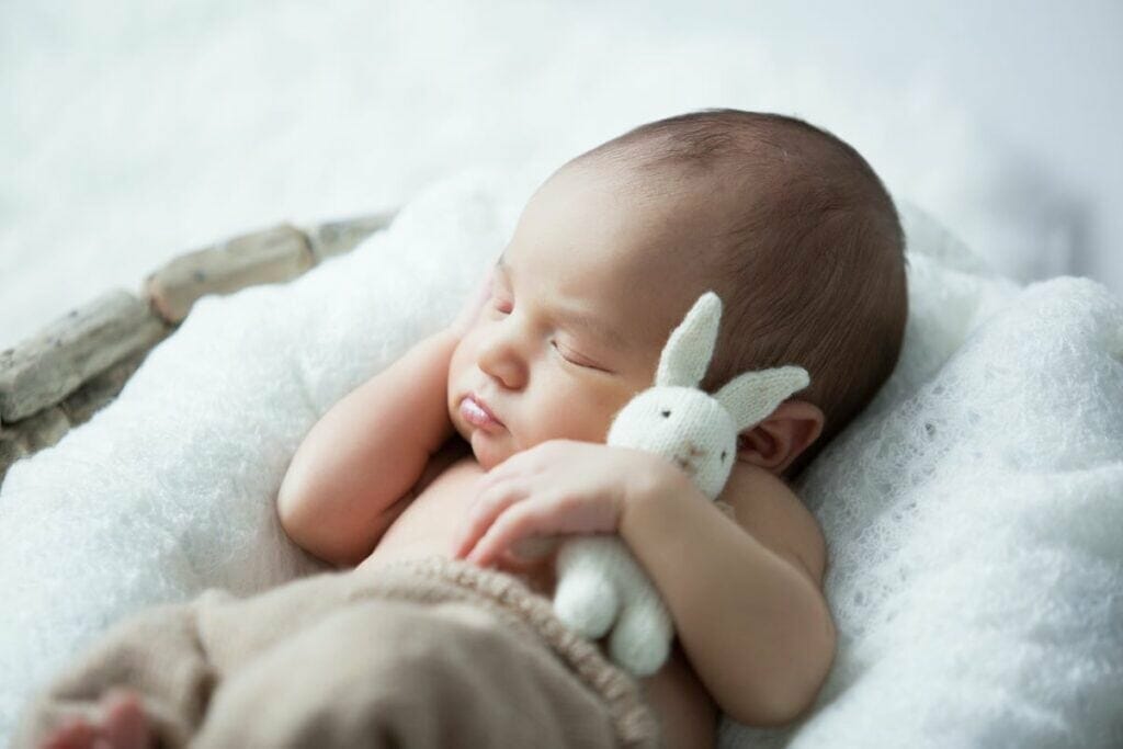 baby clutching white rabbit toy while asleep