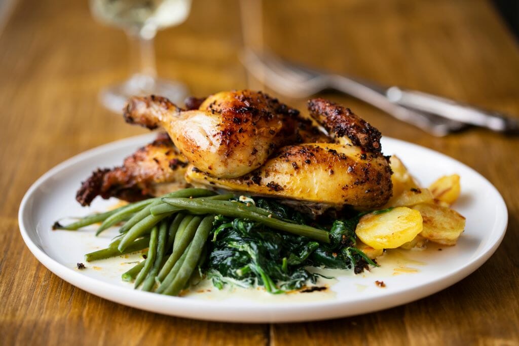 Plate of roasted poussin with potatoes, mashed swede, green beans and creamy spinach